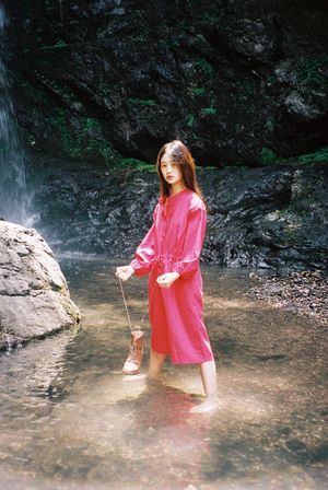 一位穿着粉红色雨衣的年轻女子站在一条溪流上的岩石上 靠近瀑布。