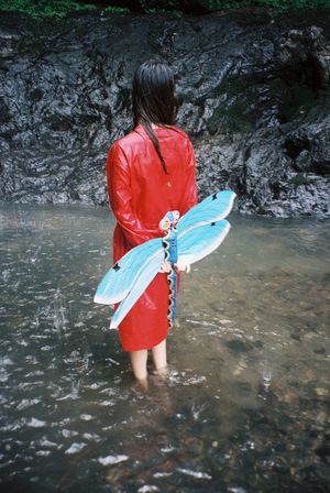 一位穿着红色雨衣的年轻女子站在河里的浅水区