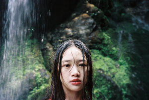 一个年轻女子站在瀑布下的丛林中 手里拿着一把雨伞。