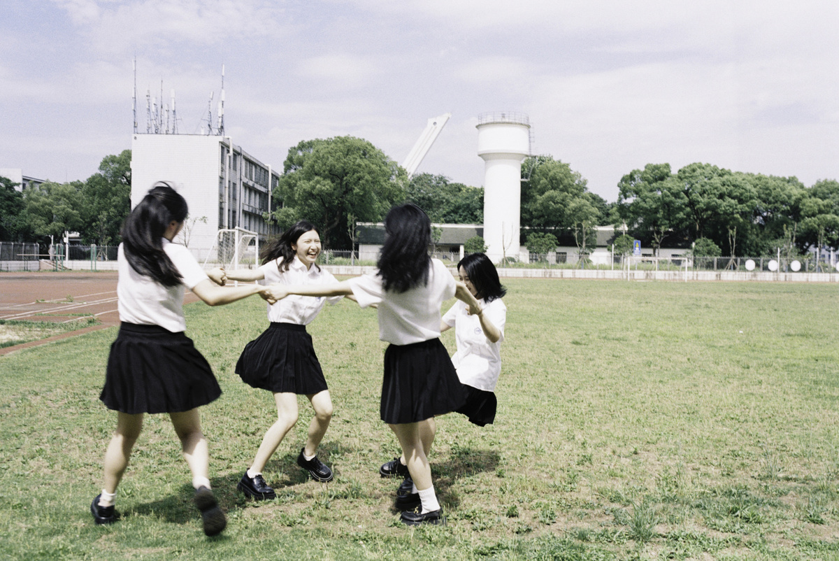 校园里的年轻女孩穿着校服手拉手在草地上