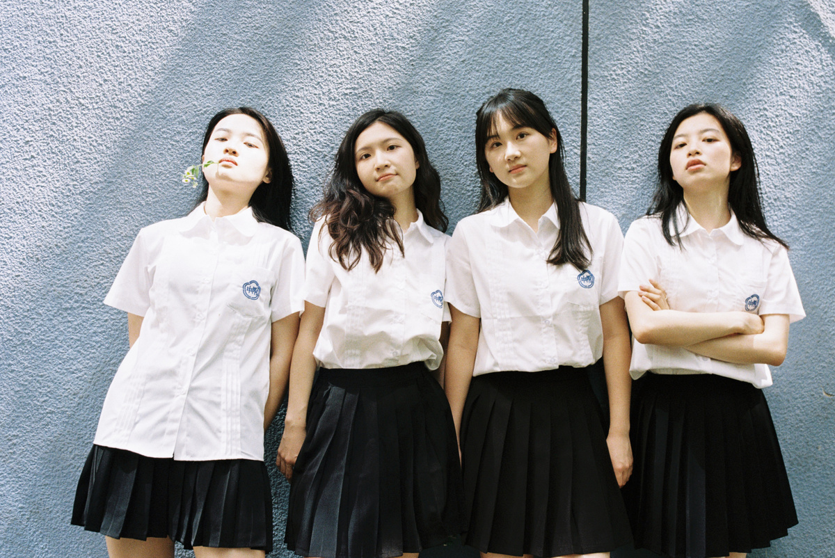 四个穿白衬衫和裙子的小女孩在蓝色墙壁前摆姿势