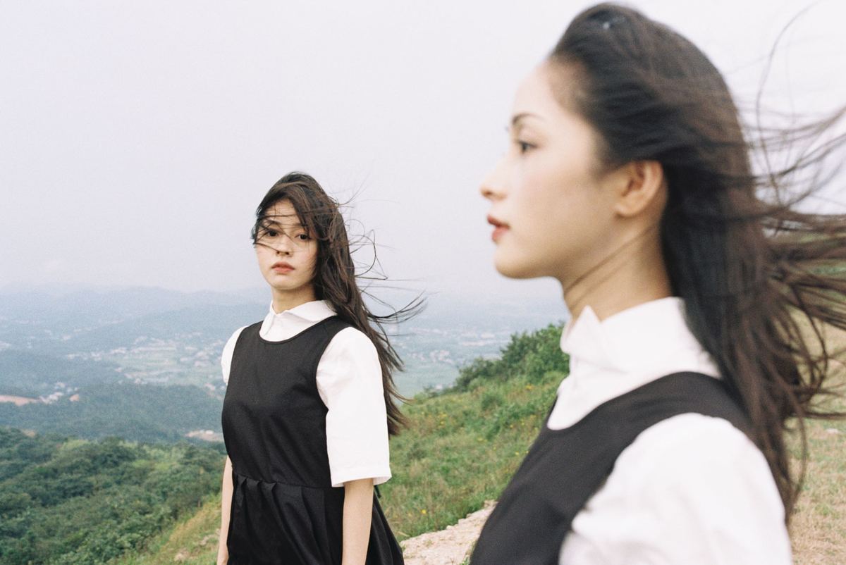 两位年轻女性站在山顶俯瞰山脚下的山谷