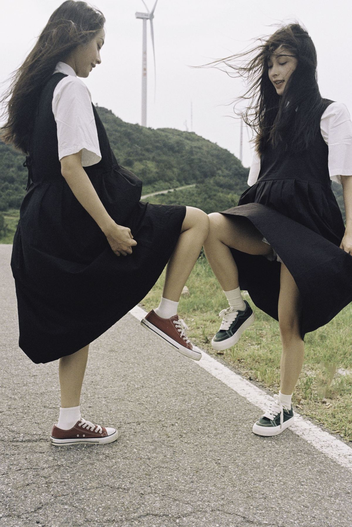 两名穿黑色连衣裙的年轻女子坐在路上。