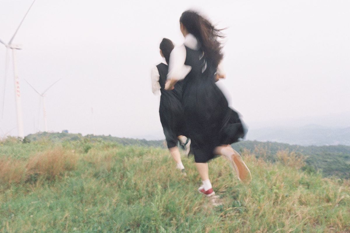 一个穿着黑色连衣裙的年轻女子在草地上奔跑 背景中有风车。