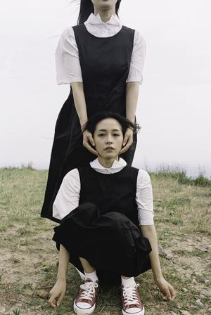一个穿着黑色连衣裙的年轻女孩坐在田野里的草地上 身后站着一位女士。