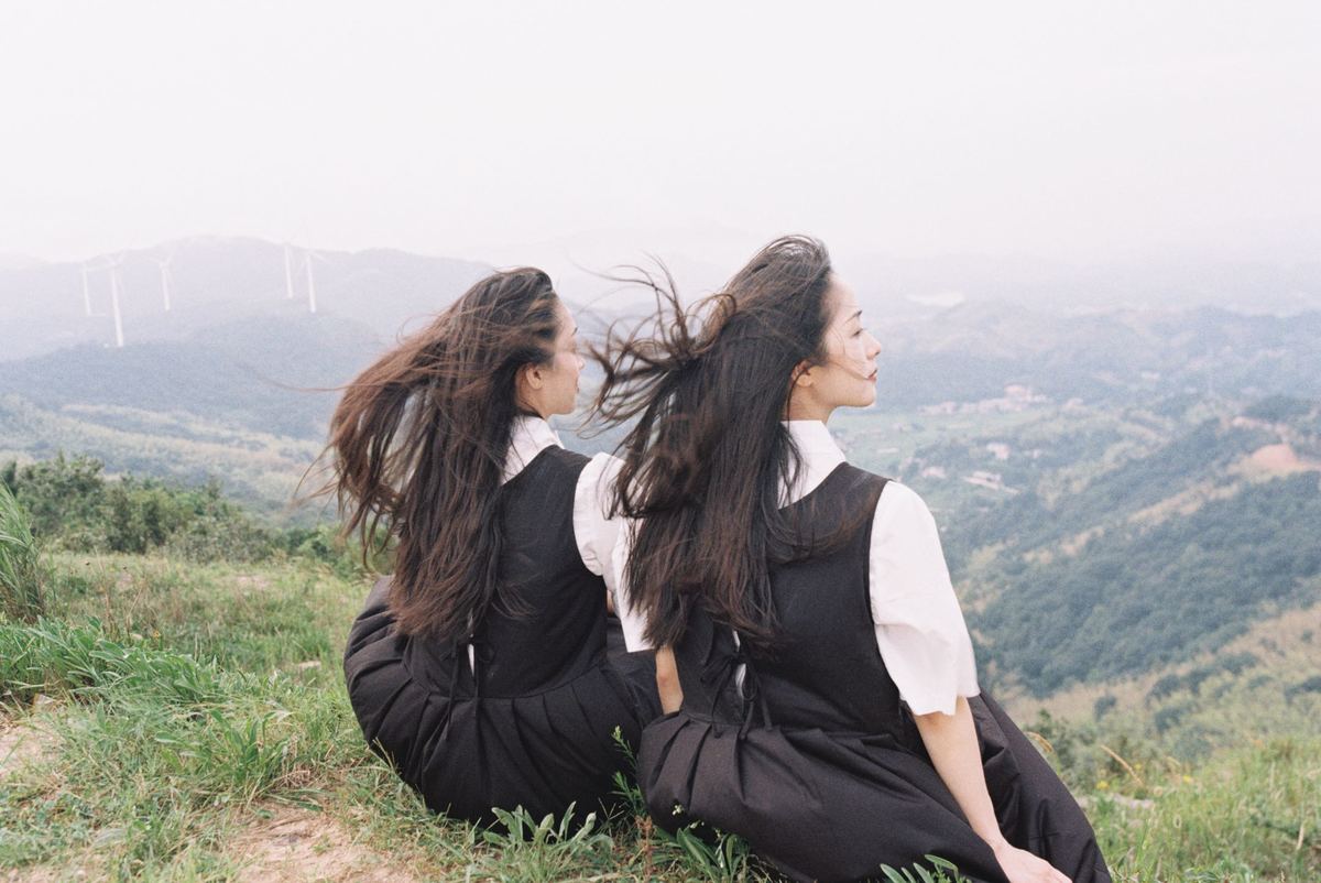 两位年轻女性坐在草地上 背景是山脉。