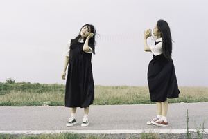 两名穿黑色连衣裙的年轻女子站在一条路的中央。