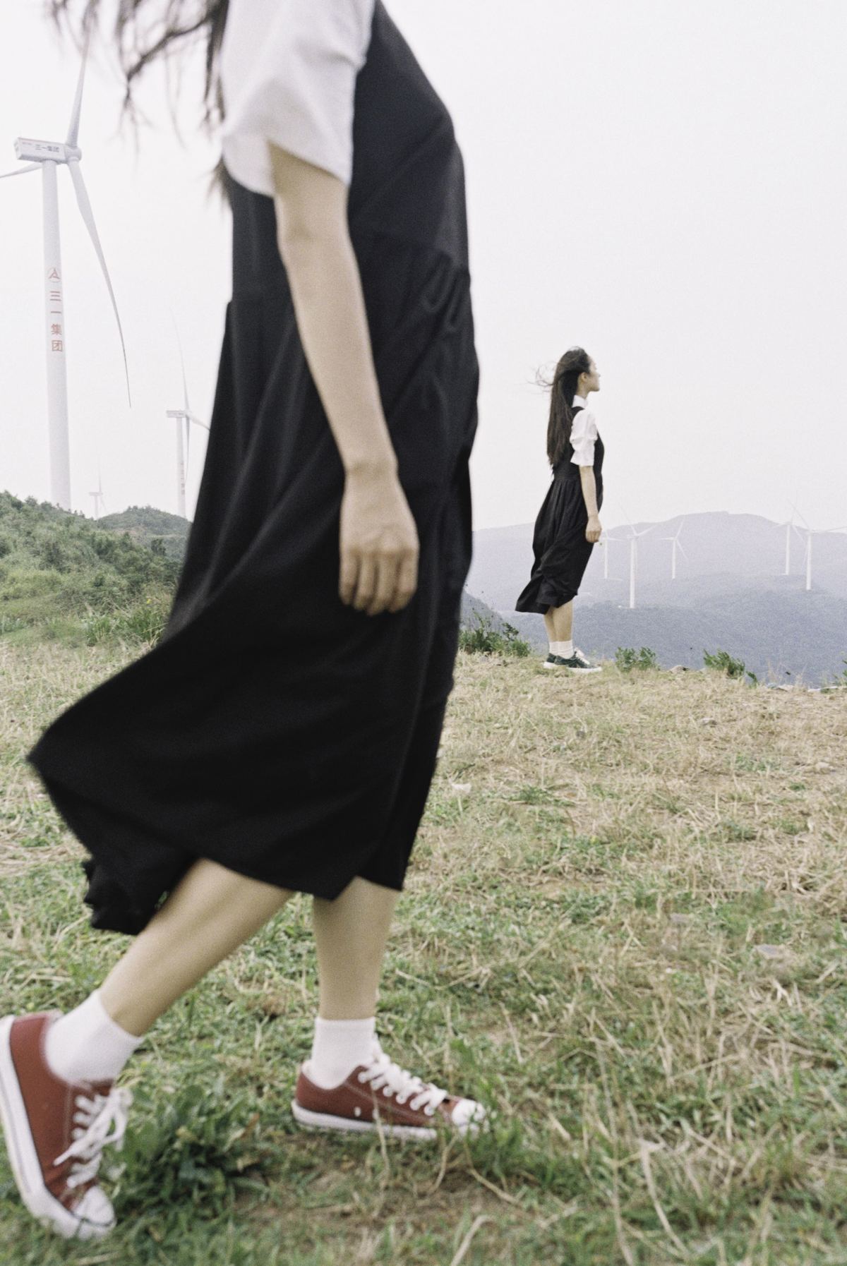 一个人穿着黑色连衣裙在草地上行走 背景是风车。