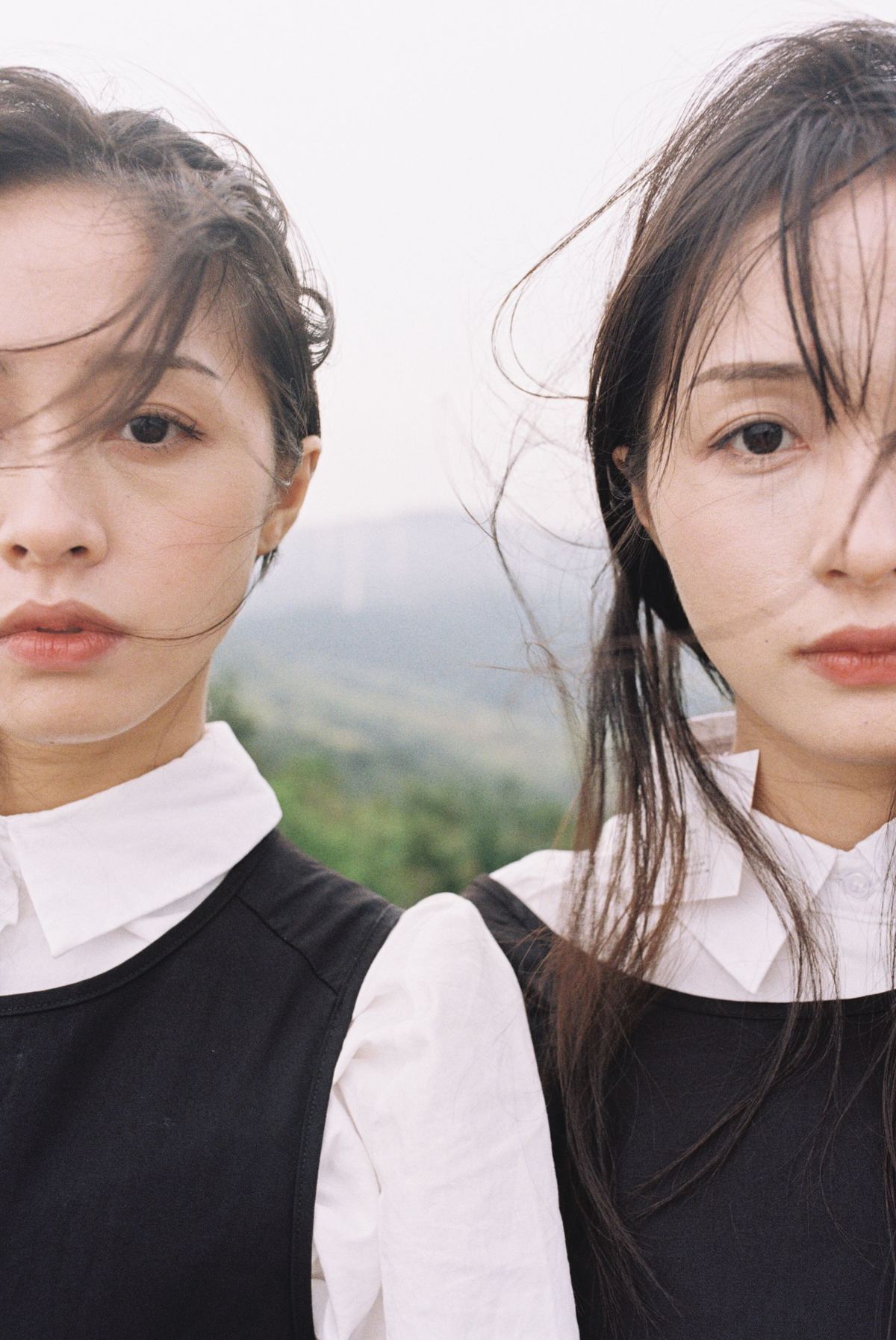 两位穿着制服的年轻女性站在山丘背景前。
