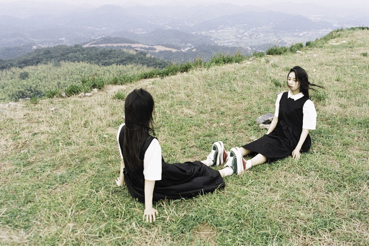 两个年轻女子坐在山顶上的草地上