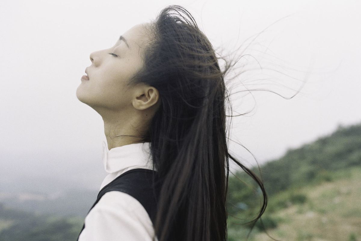 一位长发飘飘的年轻女子站在山丘上 任风吹动。