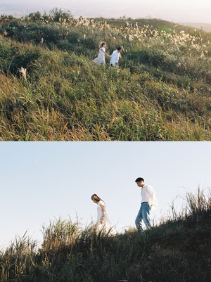 一张照片 一对夫妇手握风筝 站在山丘上 山丘的另一边 一个孩子在草地上玩耍。