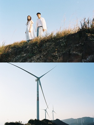 一个男人和一个女人站在一个山丘上 旁边有一个风力发电厂 背景中有风车。