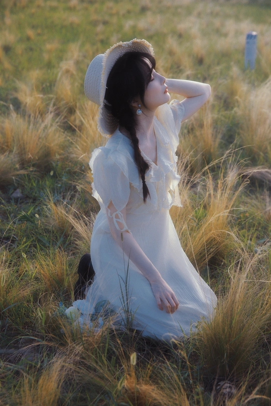 一位穿着白色裙子和帽子坐在田野里的年轻女子