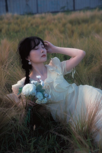 一位美丽的年轻女士穿着白色裙子坐在草地上 地上铺满了鲜花。