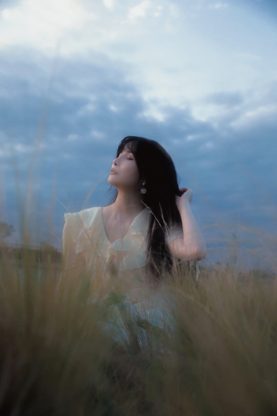 一个穿着白色连衣裙的年轻女子坐在高草丛中