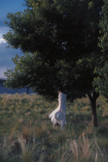 一位穿着白色连衣裙的女性拿着飞盘站在一棵大树旁的草地上