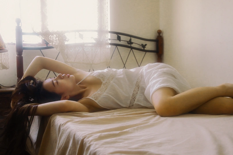 一个穿着白色连衣裙的年轻女子躺在靠近窗户的床上