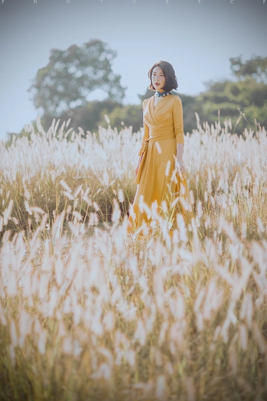 一位穿着黄色连衣裙的年轻女子站在一片高草丛中。