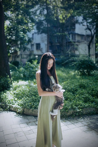 穿绿色连衣裙的年轻女子抱着一只猫在走