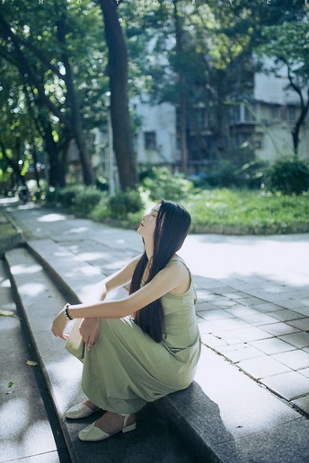 一位穿着绿色连衣裙的年轻女子坐在公园的长椅上