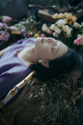 一个穿着连衣裙的年轻女子躺在椅子上 周围有花和植物。