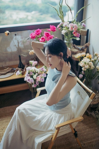 一个穿着白色连衣裙的年轻女子坐在椅子上 头戴花环 凝视着窗外。