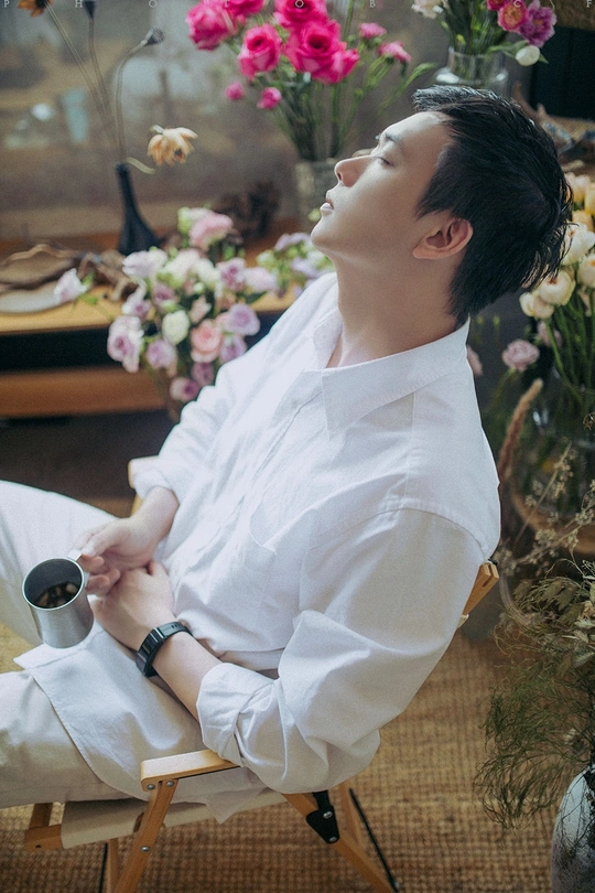 一个穿着白衬衫的年轻人坐在一把椅子上 手里拿着一杯咖啡和一支香烟。