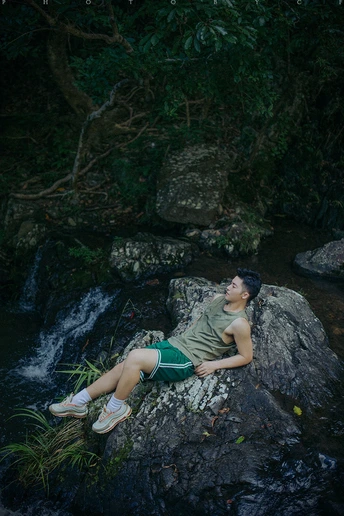 一个穿着绿色T恤的年轻男子坐在一条河或小溪中的岩石上