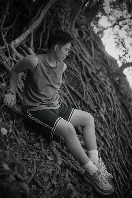 一个年轻男子坐在森林中的一棵树的根部 黑白照片。