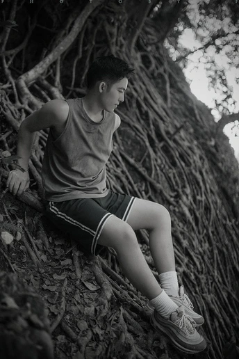 一个年轻男子坐在森林中的一棵树的根部 黑白照片。