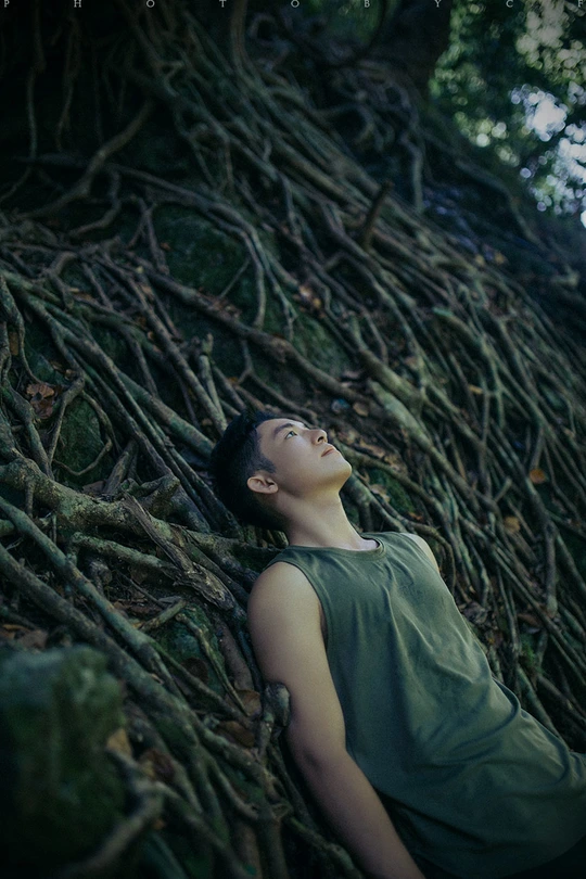 一位年轻女子躺在森林中的一堵根墙的根部 而另一个女孩则躺在背景中。