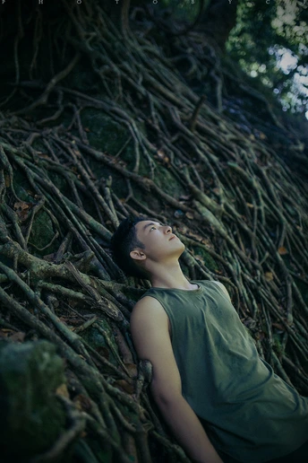 一位年轻女子躺在森林中的一堵根墙的根部 而另一个女孩则躺在背景中。