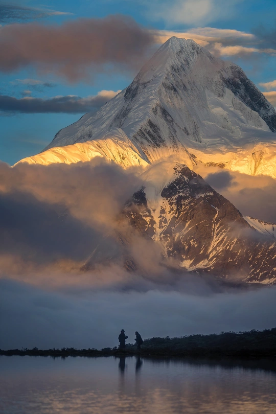 夕阳下在湖边钓鱼的 couple of people 和背景中的山