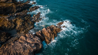 岩石海岸线的空中视角 岸边有一座灯塔 海洋中的岩石被波涛拍打 晴空下蔚蓝的天空。