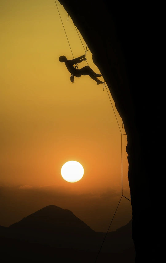 日落时一个男子攀登山顶的剪影