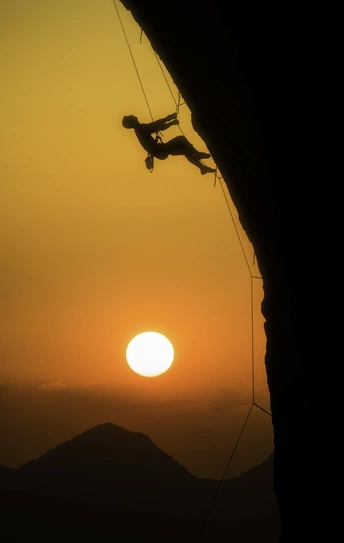 日落时一个男子攀登山顶的剪影