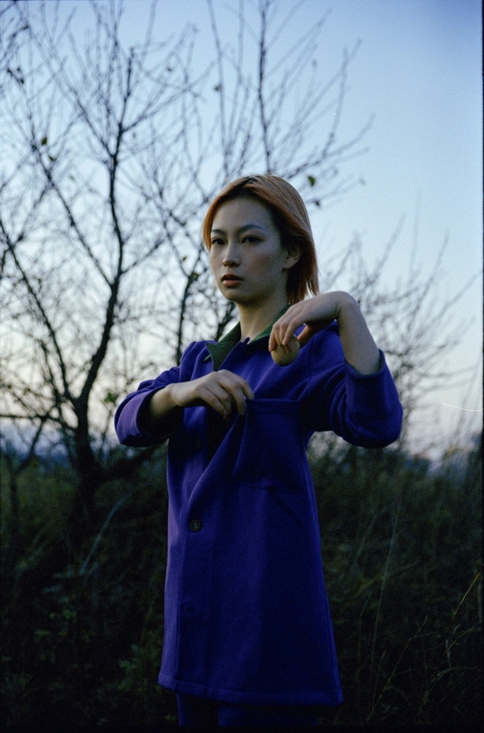 一位穿着蓝色外套的年轻女子站在一个有树木背景的田野中