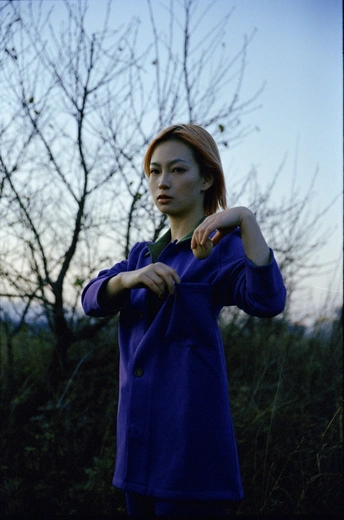 一位穿着蓝色外套的年轻女子站在一个有树木背景的田野中