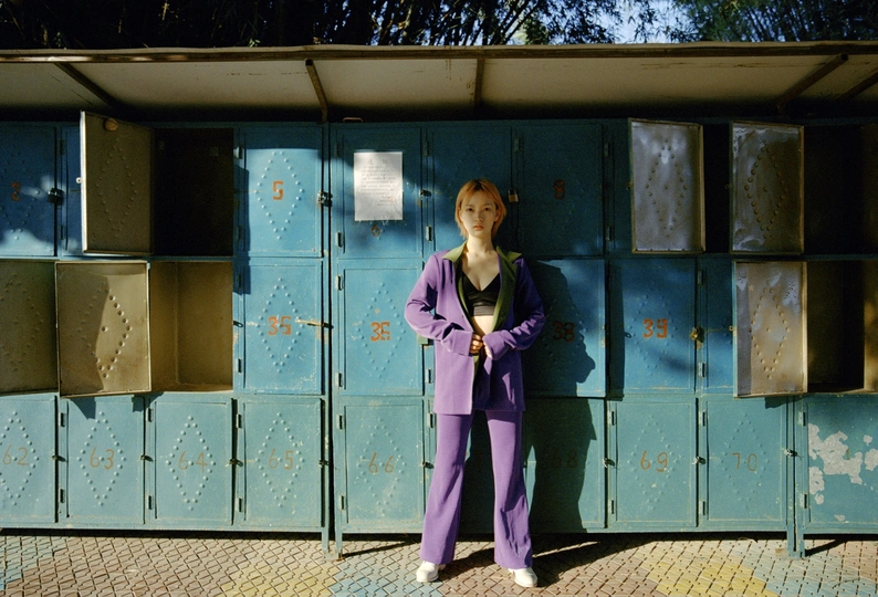 一位穿着紫色西装的女性站在一排厕所和箱子前面