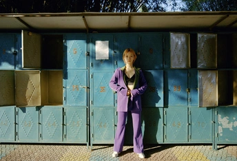 一位穿着紫色西装的女性站在一排厕所和箱子前面