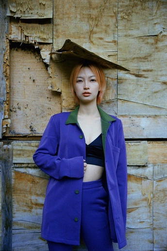 一位穿着蓝色外套和绿色夹克站在木墙前面的女人