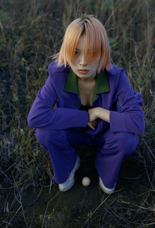 一位戴绿色头发的女孩穿着紫色套装坐在草地上