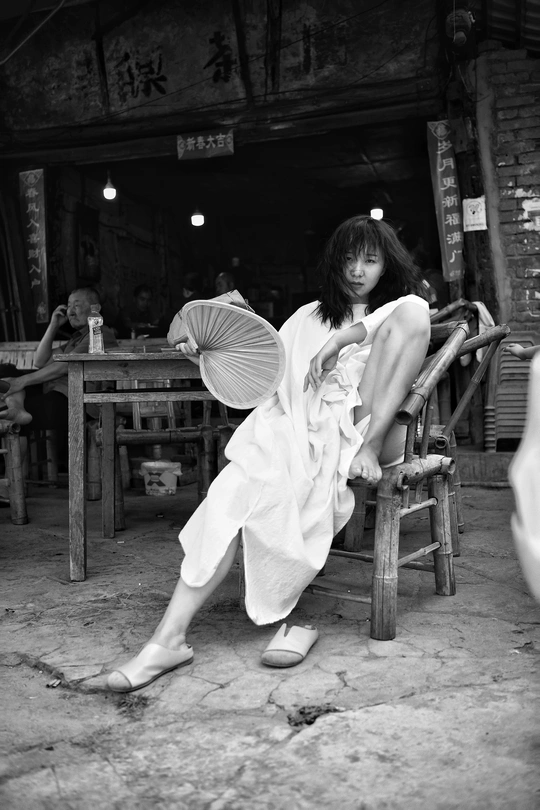 一张黑白照片 一位年轻女士穿着白色裙子坐在木椅上