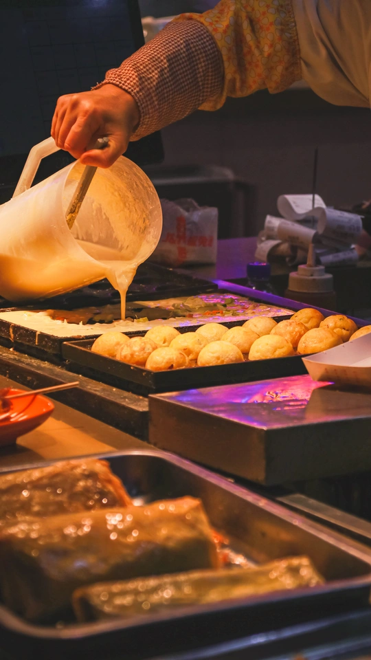 一个男人正在厨房里往锅里倒面糊 盘子里放着一些甜点。