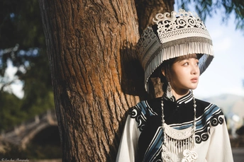 一位穿着传统服装的年轻女孩站在一棵树旁 戴着帽子。