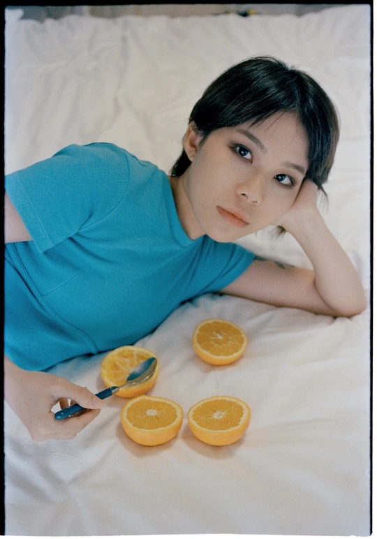 一个穿着蓝色衬衫的年轻女人躺在床上切桔子