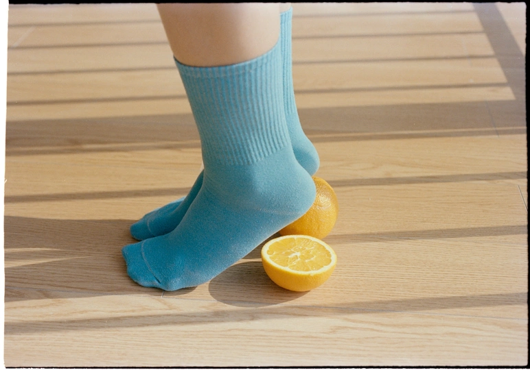 一个人的腿穿着蓝色袜子 坐在地板上 手里拿着柠檬和橙子