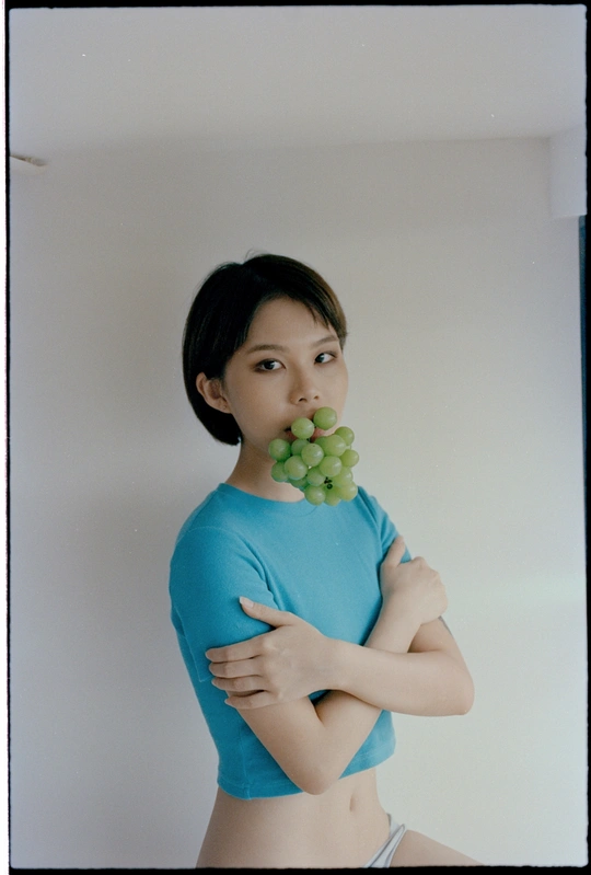 一个穿着蓝色衬衫的年轻女子把绿色葡萄举到脸上