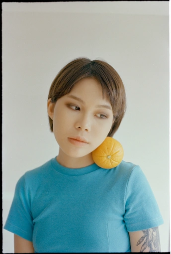 一个穿着蓝色衬衫的年轻女孩脸上拿着一个桔子